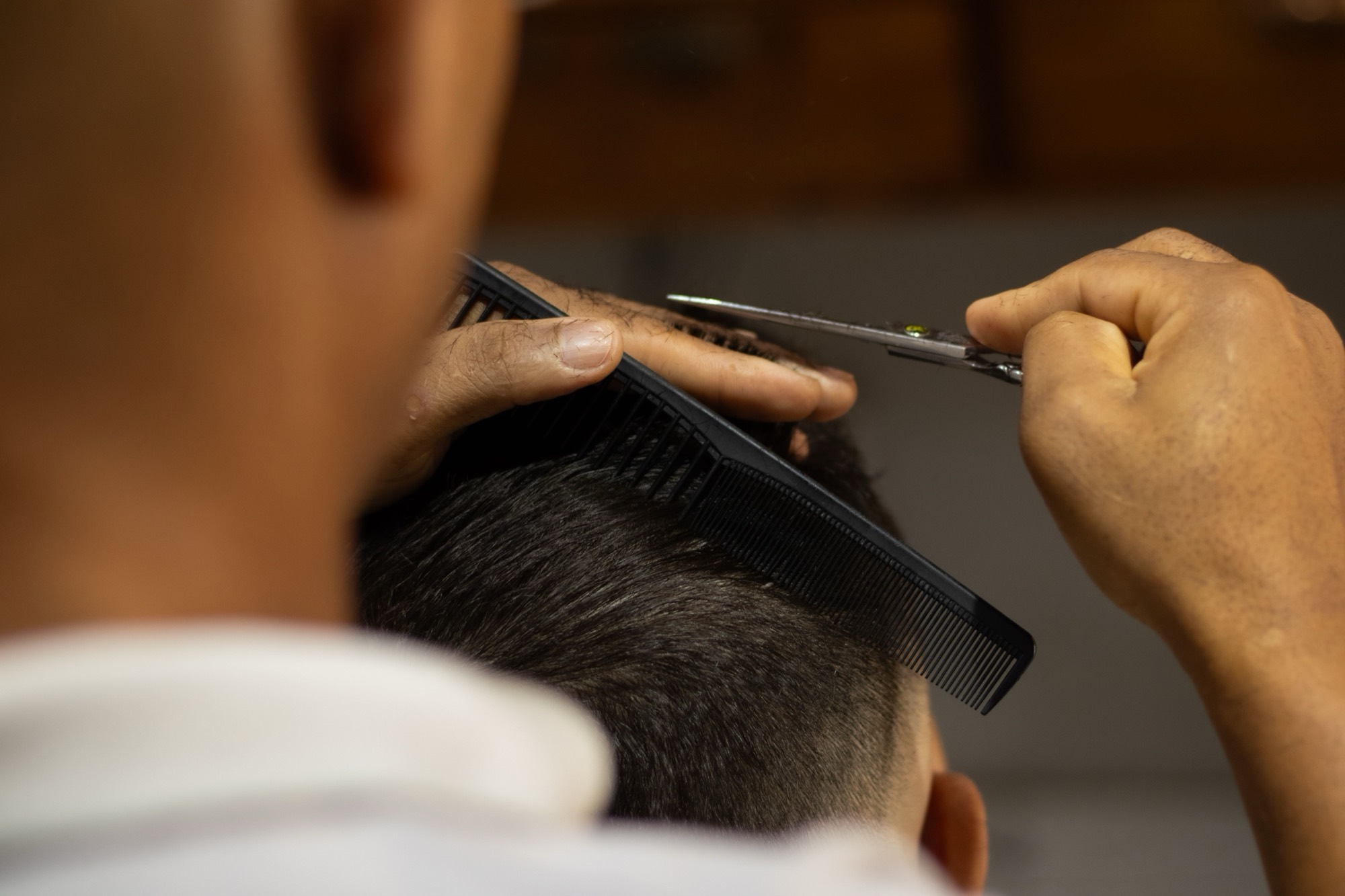 A barber cutting a client’s hair with scissors and a comb