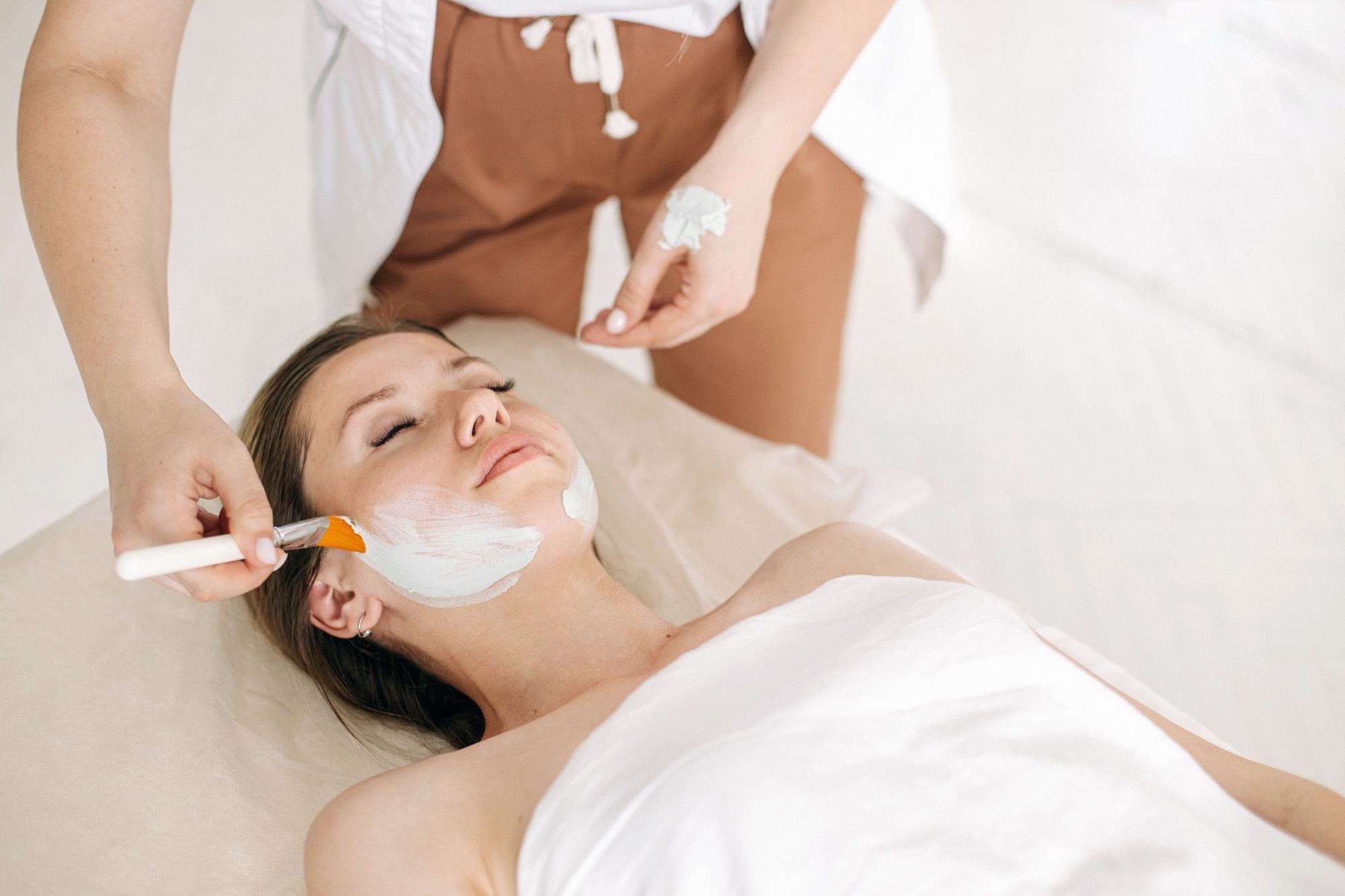 An esthetician applying a facial mask with a brush