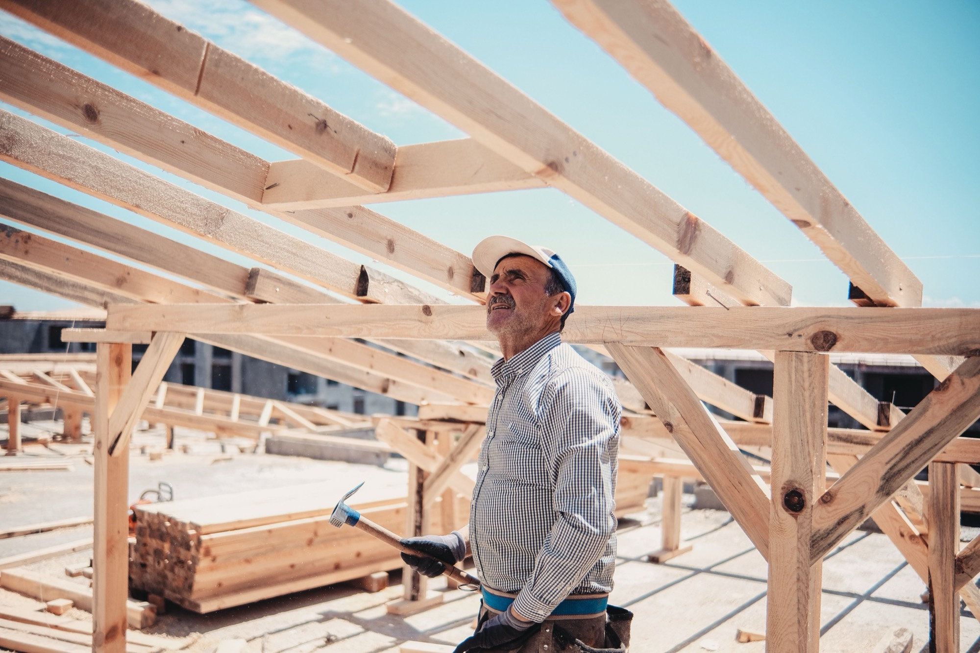 A carpenter framing the roof of a new house against a blue sky
