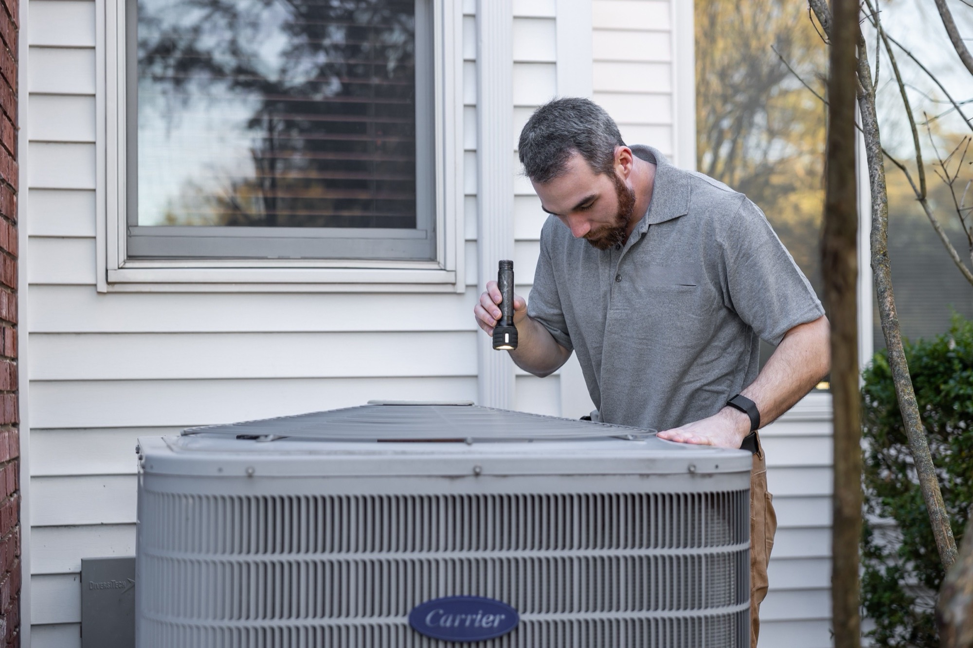 An HVAC technician servicing an outdoor air conditioning unit beside a house