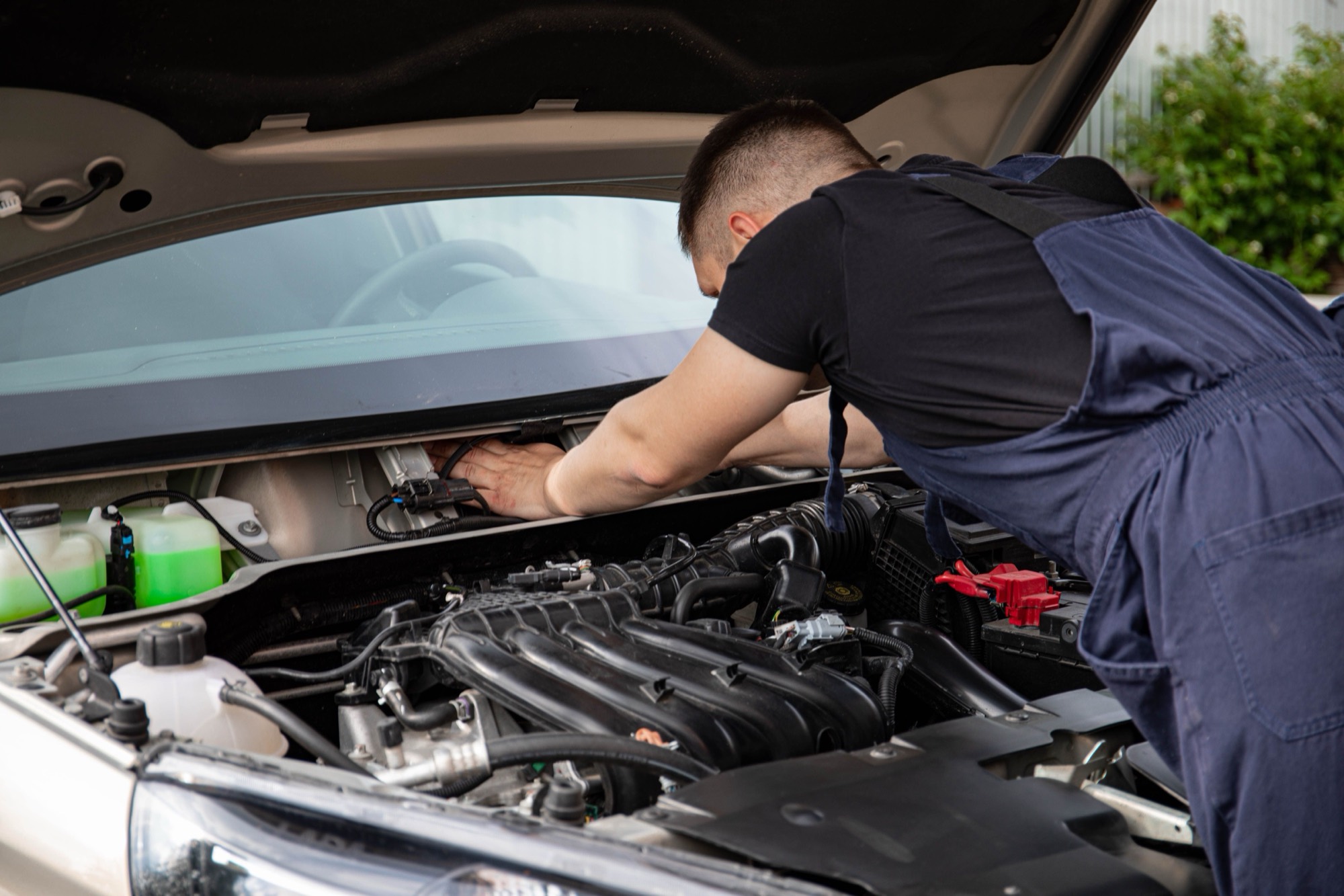 A mechanic working under the open hood of a car