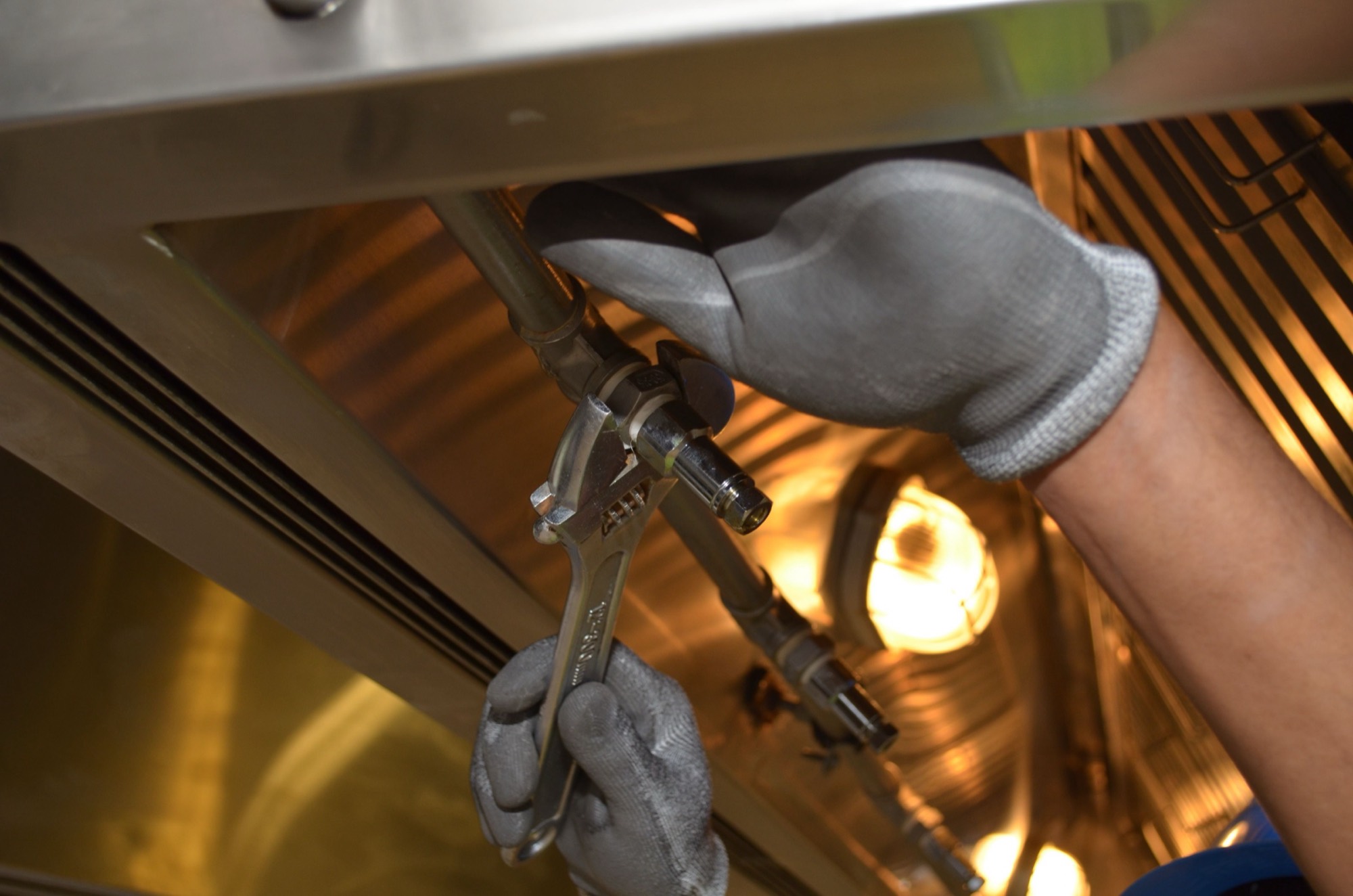 A plumber’s gloved hands tightening a pipe fitting with a wrench under warm light